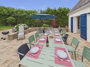A dining table set outdoors with chairs, a grill, and a potted plant.