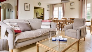 A living room with a sofa, armchairs, a glass coffee table, and a dining area with a table and chairs. - 800 m from harbour – House terrace BBQ – Sleeps 12 (Loctudy)
