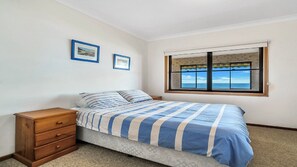 A bedroom with a bed, a wooden dresser, two framed pictures on the wall, and a window with a view.