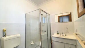 Ein Badezimmer mit einer Duschkabine, Toilette, Waschbecken mit Spiegel und einem Fenster über dem Waschbecken.