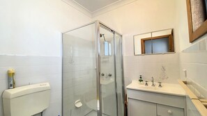 Un bagno con doccia vetro, toilette, lavandino con specchio e finestra sopra il lavandino.