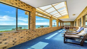 A sunlit room with large windows, a brick wall, and a blue floor. - Minnie Water Beach House (Minnie Water)