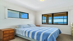 Ein Schlafzimmer mit einem Bett, einem Nachttisch, einer Kommode und zwei Fenstern mit Blick.