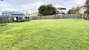 A backyard with a wooden fence, a grassy lawn, and a house in the background. - Minnie Water Beach House (Minnie Water)