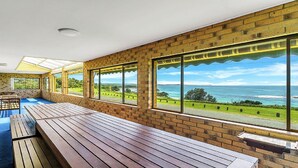 Ein überdachter Außenbereich mit Holzbänken und großen Fenstern mit Blick auf eine Küstenlandschaft.