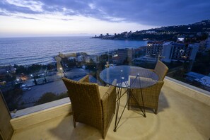 A balcony with wicker chairs and a glass table overlooking a coastal cityscape at dusk. - ZETT HOTEL (Jounieh)