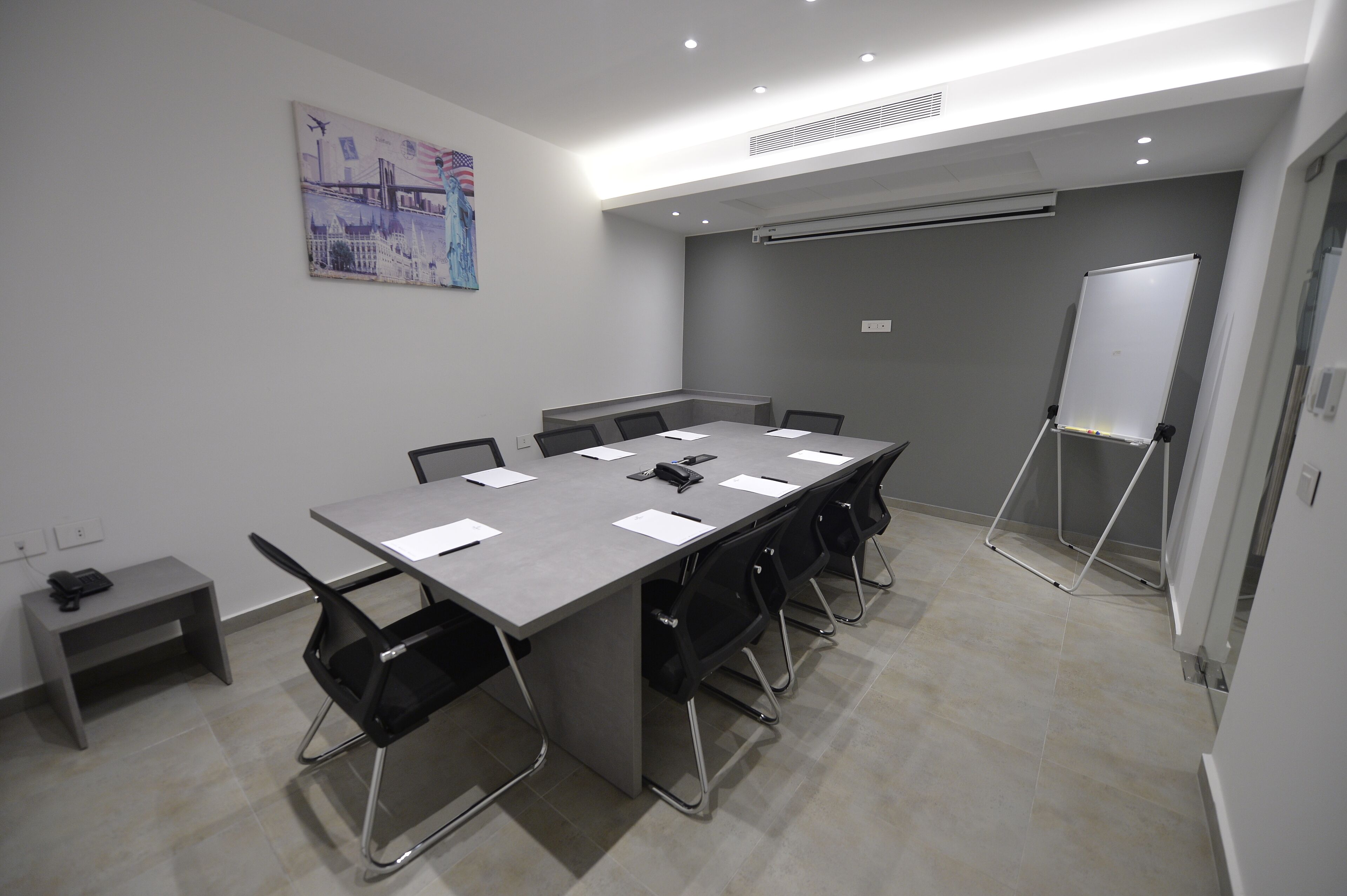 Une salle de conférence avec une longue table, des chaises noires, un tableau blanc et un tableau accroché au mur.