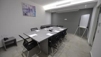 Un salón de conferencias con una mesa larga, sillas negras, una pizarra y un cuadro en la pared.