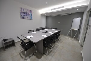 Un salón de conferencias con una mesa larga, sillas negras, una pizarra y un cuadro en la pared.
