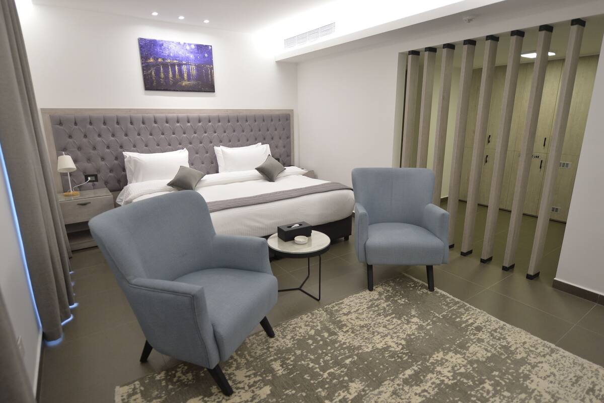 Una habitación de hotel moderna con una cama grande, dos sillones, una mesita auxiliar y un cuadro en la pared.