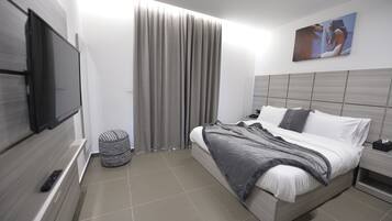 A modern hotel room with a bed, a TV mounted on the wall, a curtain, and a painting on the wall.