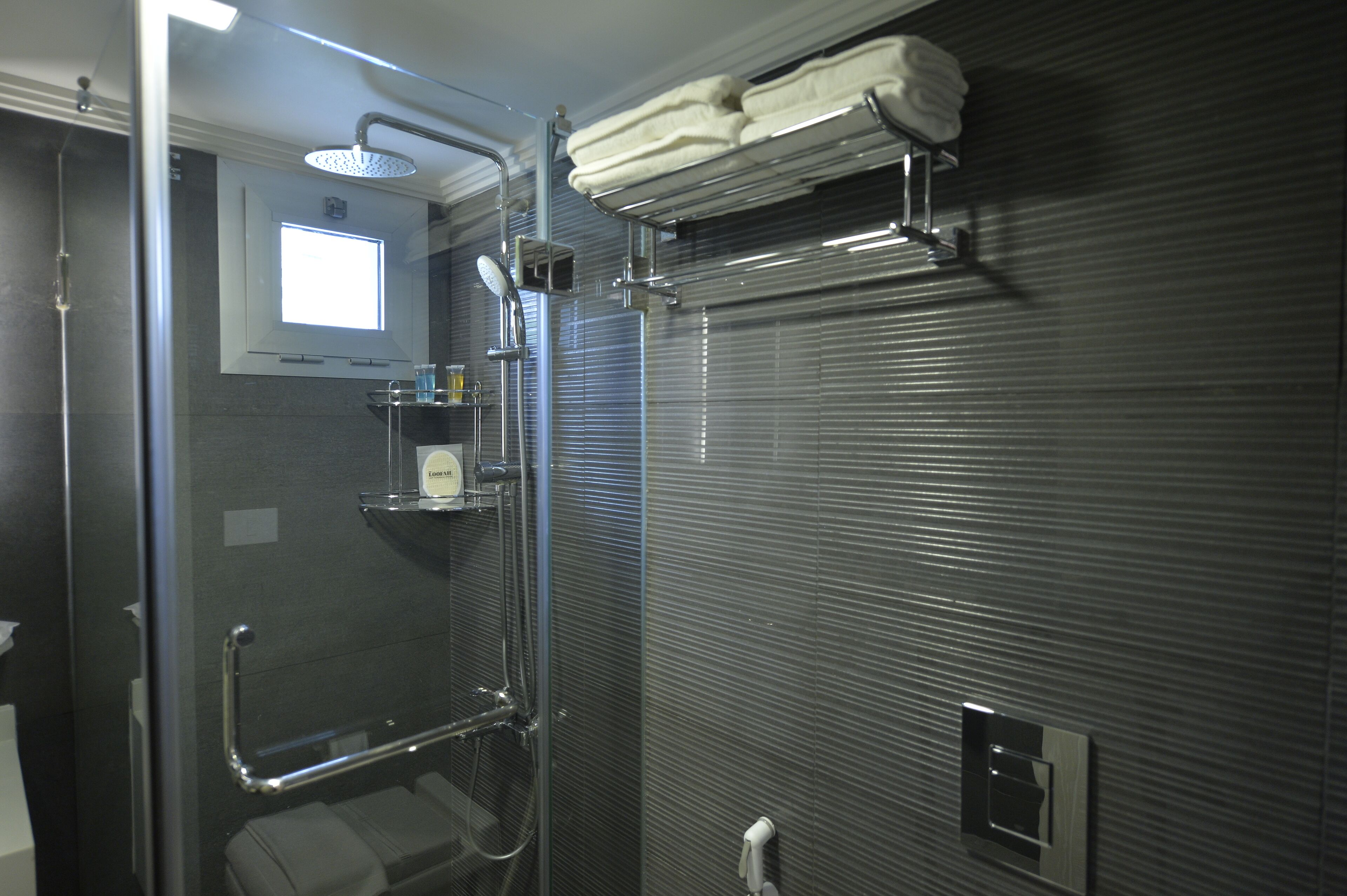A shower area with a glass door, a towel rack, and a small window.