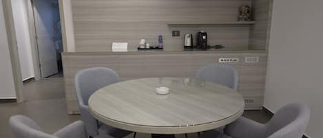 A modern kitchen with a round table and grey chairs, a coffee machine, and a mini fridge.