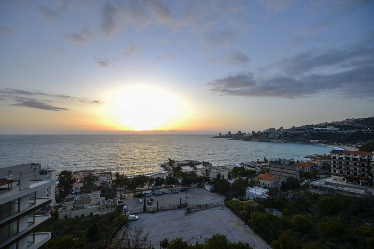 Un paisaje urbano costero al atardecer, con edificios, un estacionamiento y vistas al mar.