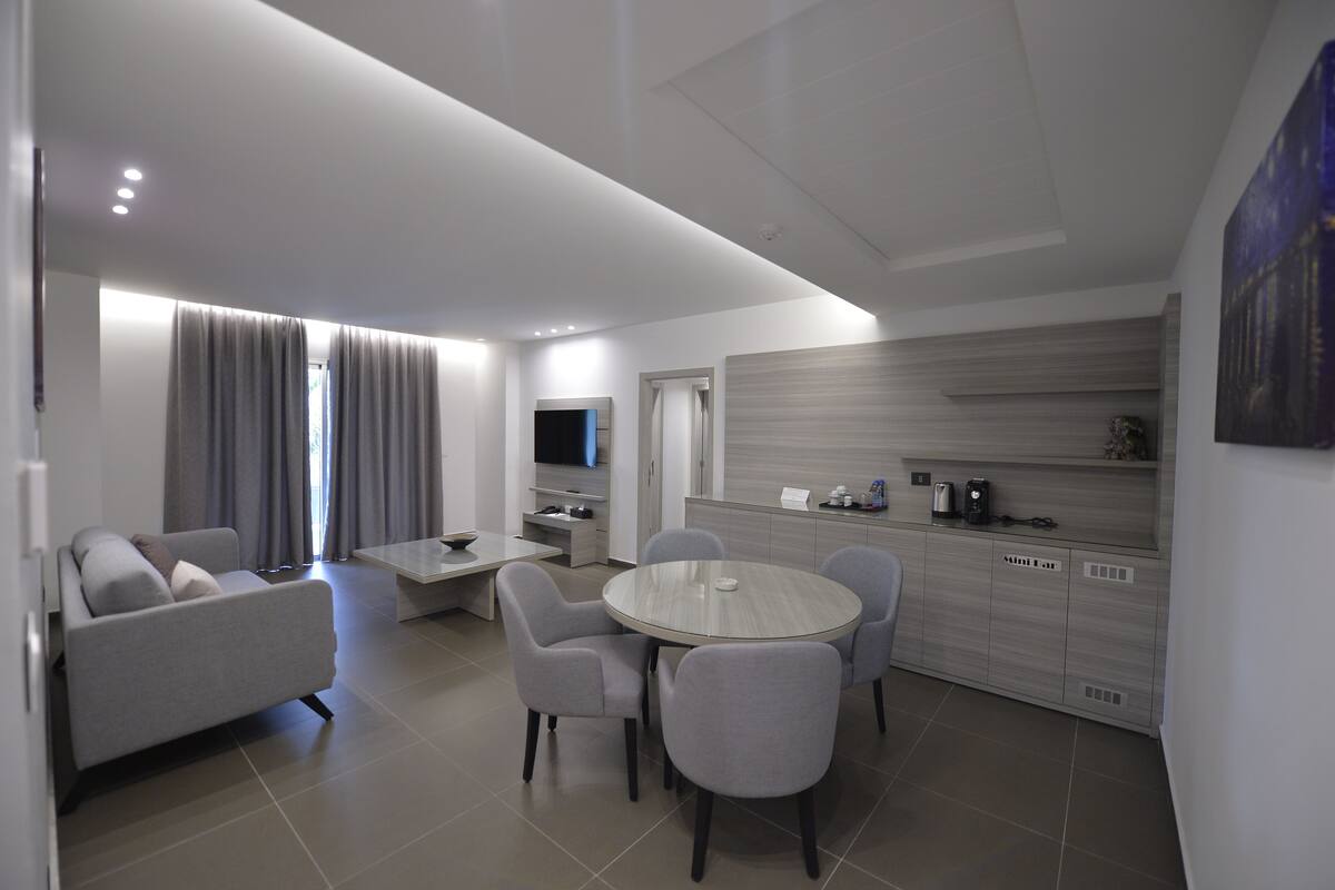Una sala de estar moderna con sofá, mesa de comedor y sillas. Cuenta con una zona de cocina con microondas, cafetera y armarios.