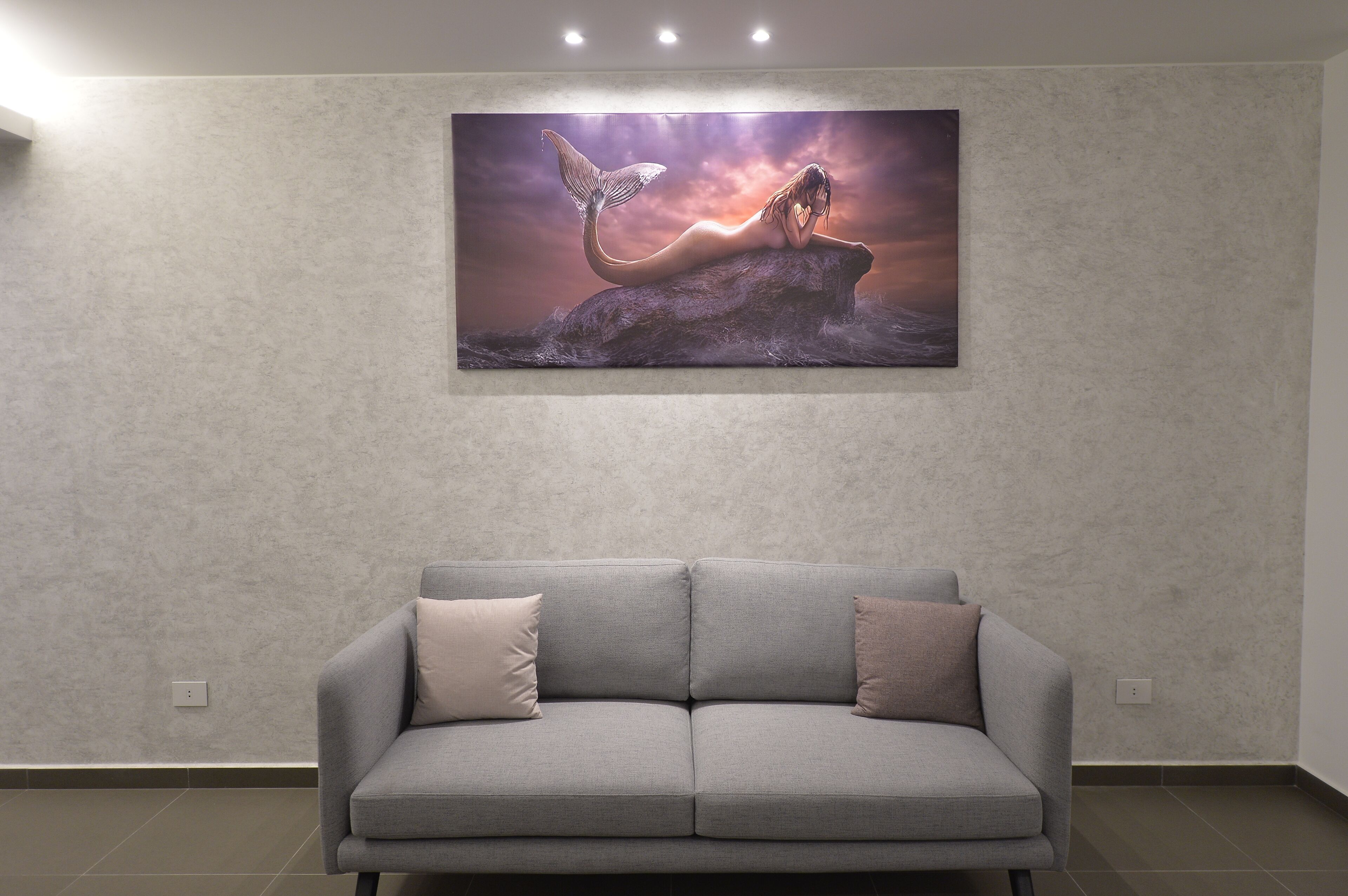 A modern living room with a grey sofa and a large abstract painting on the wall.