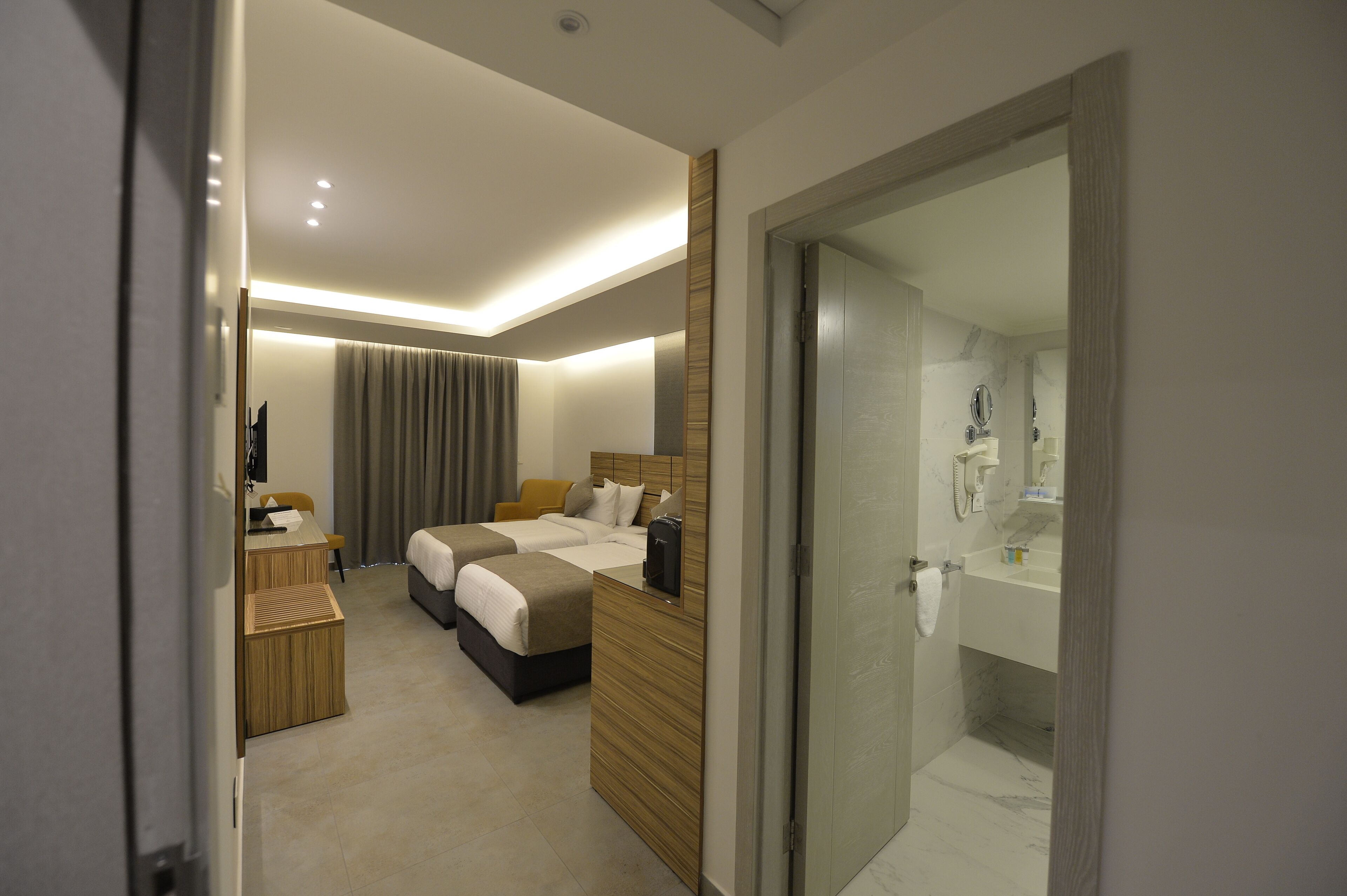 A hotel room with a bed, bedside table, lamp, and a bathroom with a mirror and sink.
