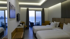 A hotel room with two beds, a desk, a chair, and a TV. There is a large window with a view of the sea. - ZETT HOTEL (Jounieh)
