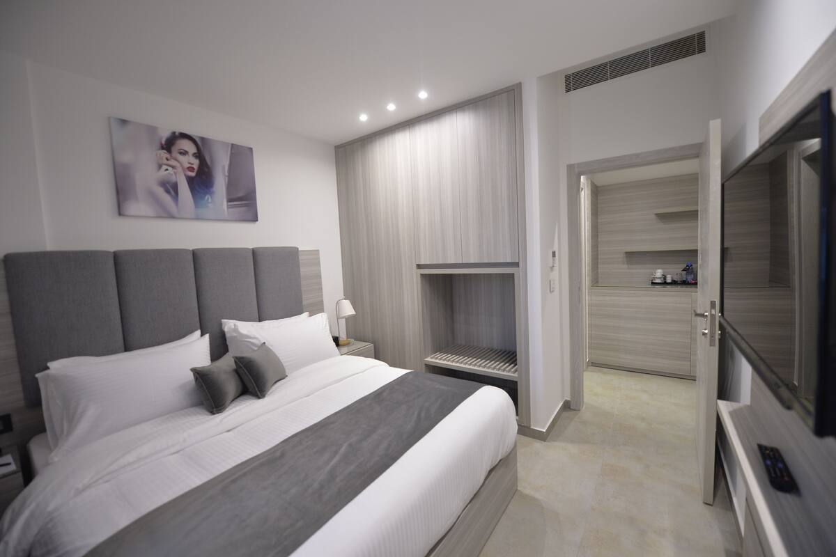 Una habitación de hotel moderna con una cama grande, un televisor de pantalla plana, un área de descanso y una puerta que da al baño.