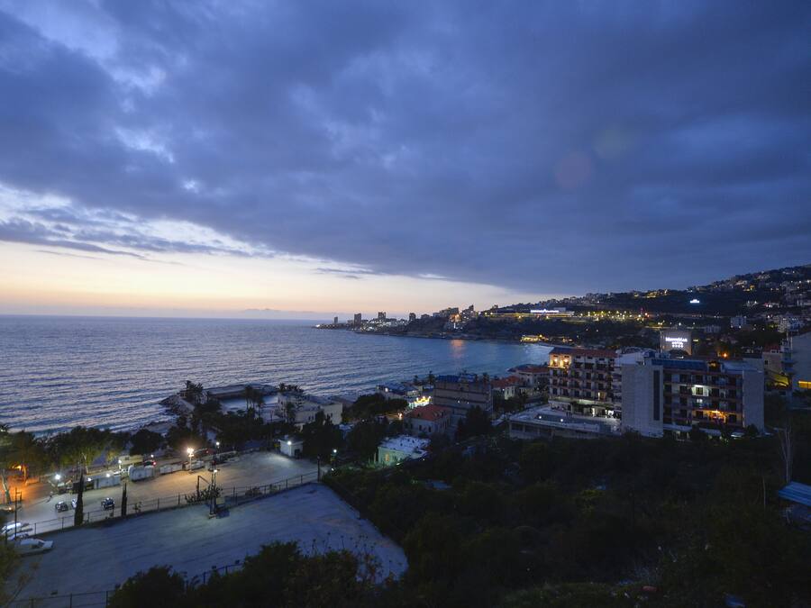 Un paisaje urbano costero al atardecer con edificios a lo largo del paseo marítimo, una carretera que lleva a la playa y una vista despejada del mar.