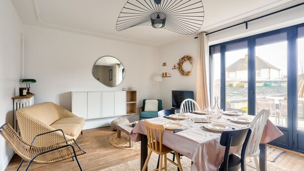 A dining area with a table set for four, a sofa, and a television in the background. - 1km Prieuré Beach - Dinard- House for 6 (Dinard)