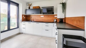 A modern kitchen with white cabinets, a black countertop, a built-in microwave, and a window providing natural light. - 1km Prieuré Beach - Dinard- House for 6 (Dinard)