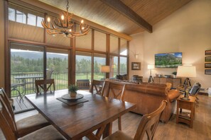 A spacious living area with a dining table, leather sofa, and a large window offering a scenic view.
