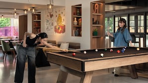 Une table de billard dans une pièce moderne, avec un canapé, une bibliothèque et une grande fenêtre.