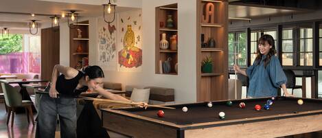 A pool table in a modern room with a sofa, a bookshelf, and a large window.