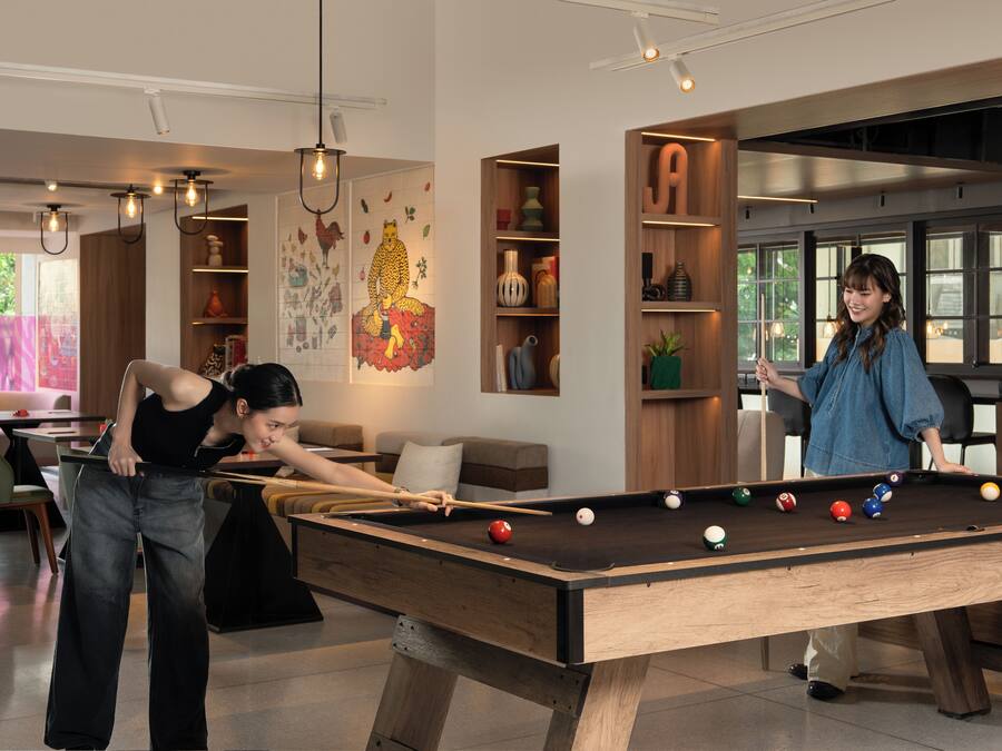 A pool table in a modern room with a sofa, a bookshelf, and a large window.