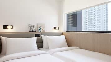 A hotel room with two beds, a wooden headboard, wall-mounted lights, and a large window with a city view.