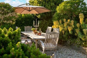 An outdoor dining area with a table and chairs, surrounded by lush greenery and flowering plants.