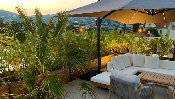 A rooftop patio with a white sofa, wooden table, and potted plants. - 27. 2-bedroom apt with balcony, private roof terrace, parking and pool (Vallauris)