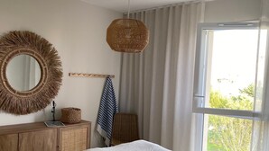 A bedroom with a bed, a round mirror, a wicker lamp, a wicker chair, and a window with curtains. - 27. 2-bedroom apt with balcony, private roof terrace, parking and pool (Vallauris)