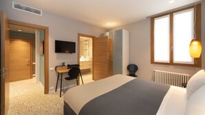 Moderni hotellihuone, jossa on sänky, työpöytä, tuoli, televisio ja ikkuna, josta on näkymä.