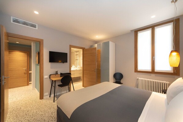A modern hotel room with a bed, a desk, a chair, a television, and a window with a view.
