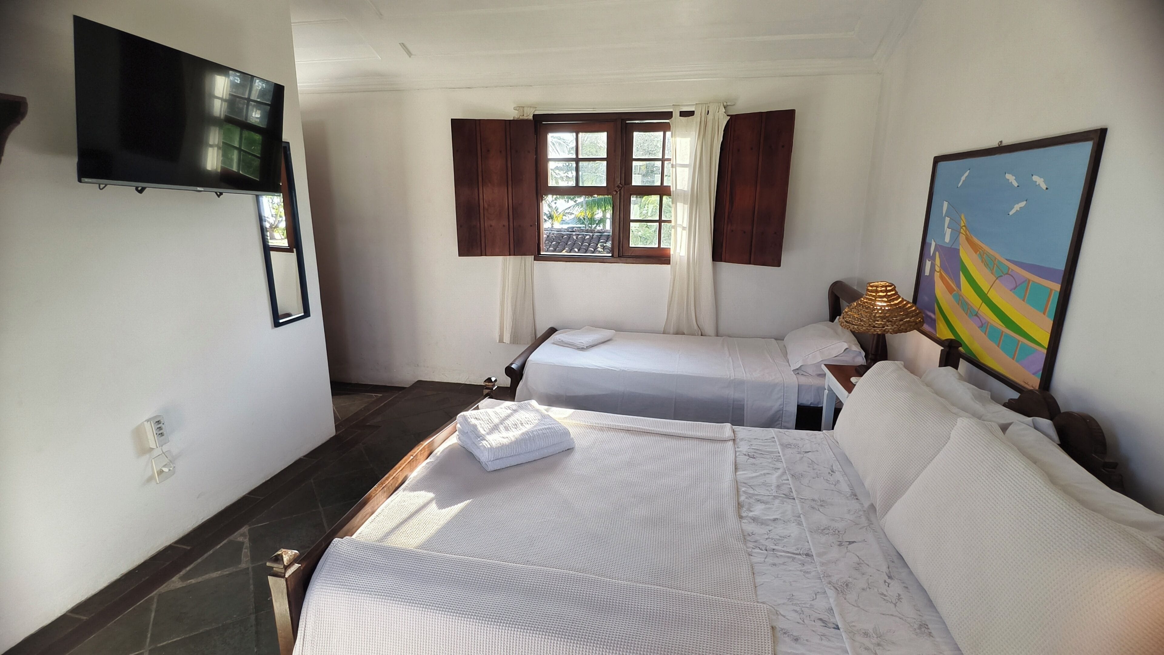 Quarto de hotel com duas camas, televisão, janela com cortinas e um quadro na parede.