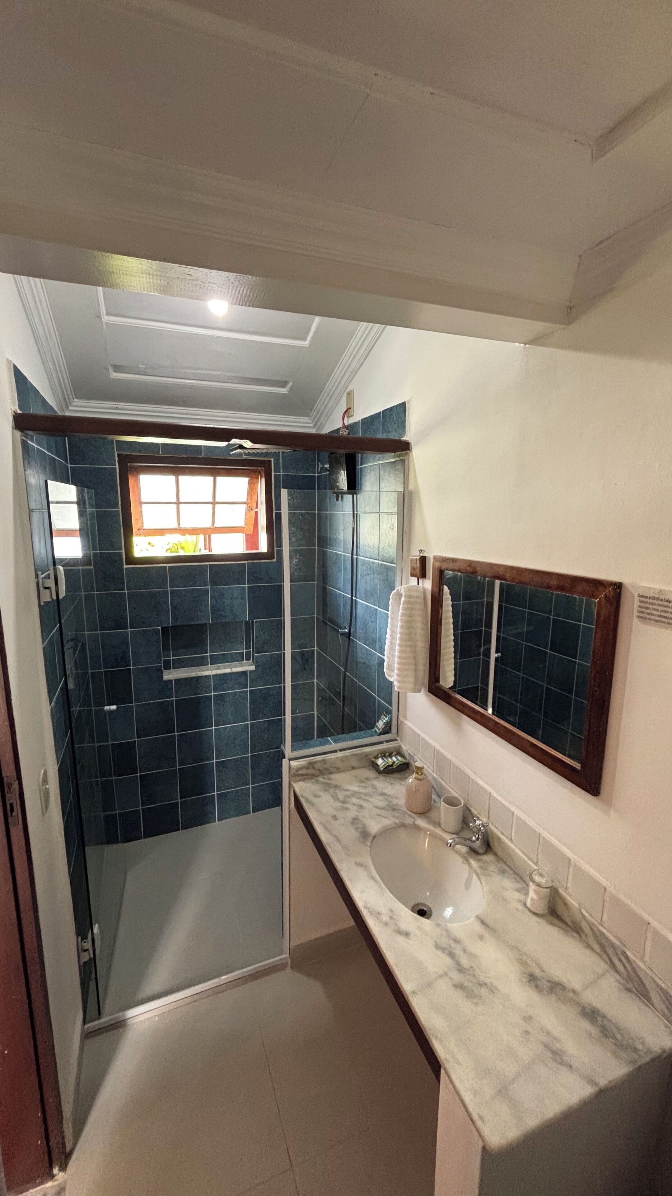 Un baño con cabina de ducha de vidrio, un lavamanos con encimera de mármol y un espejo con marco de madera.