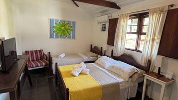 Una habitación con cama, una silla, una mesa, televisión, ventilador de techo y ventana con cortinas.