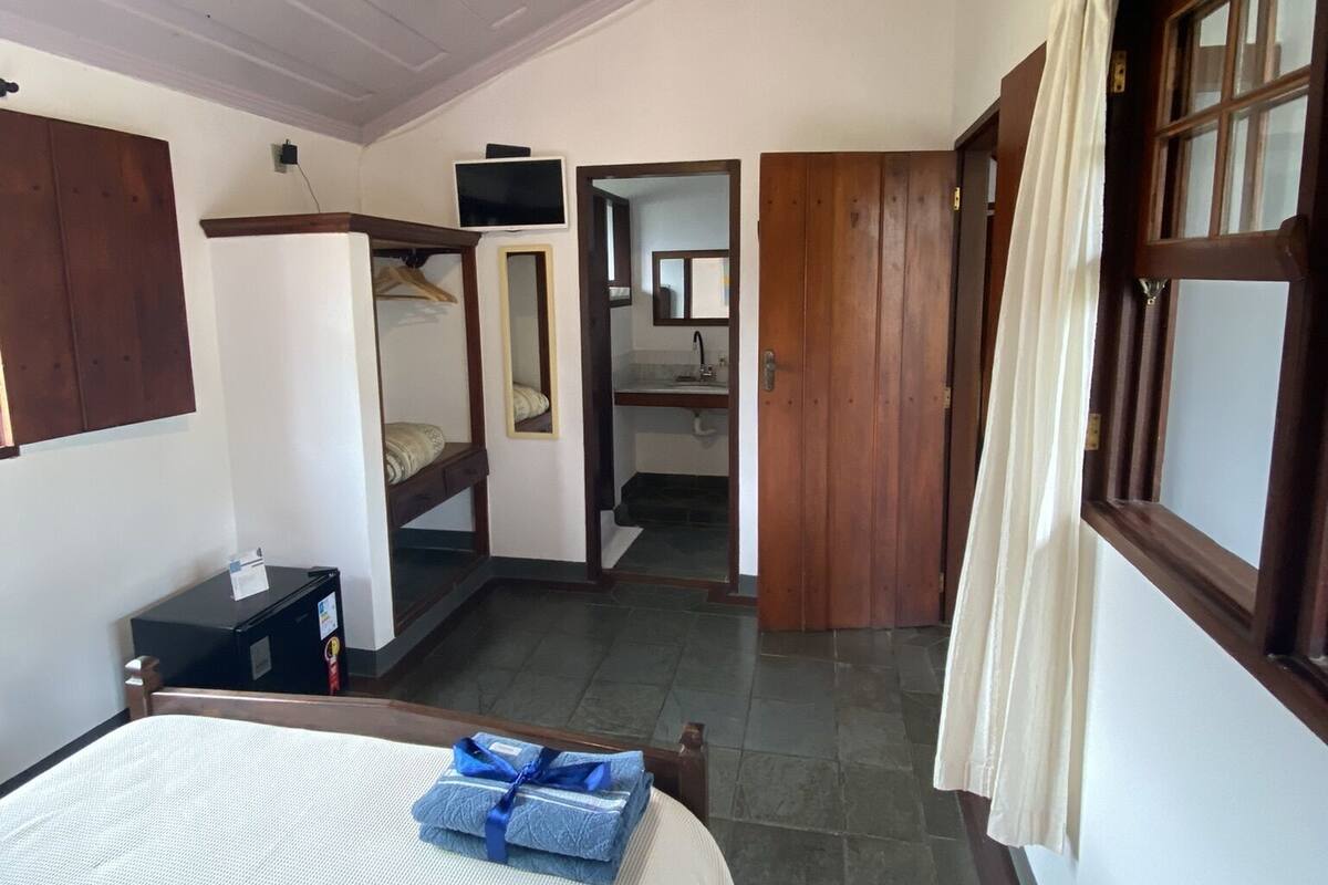 Un dormitorio con cama, ventilador de techo, televisión, armario y baño visible a través de una puerta abierta.