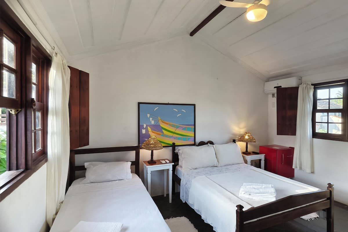 Una habitación con dos camas individuales, un cuadro en la pared, un ventilador de techo y una ventana con cortinas.