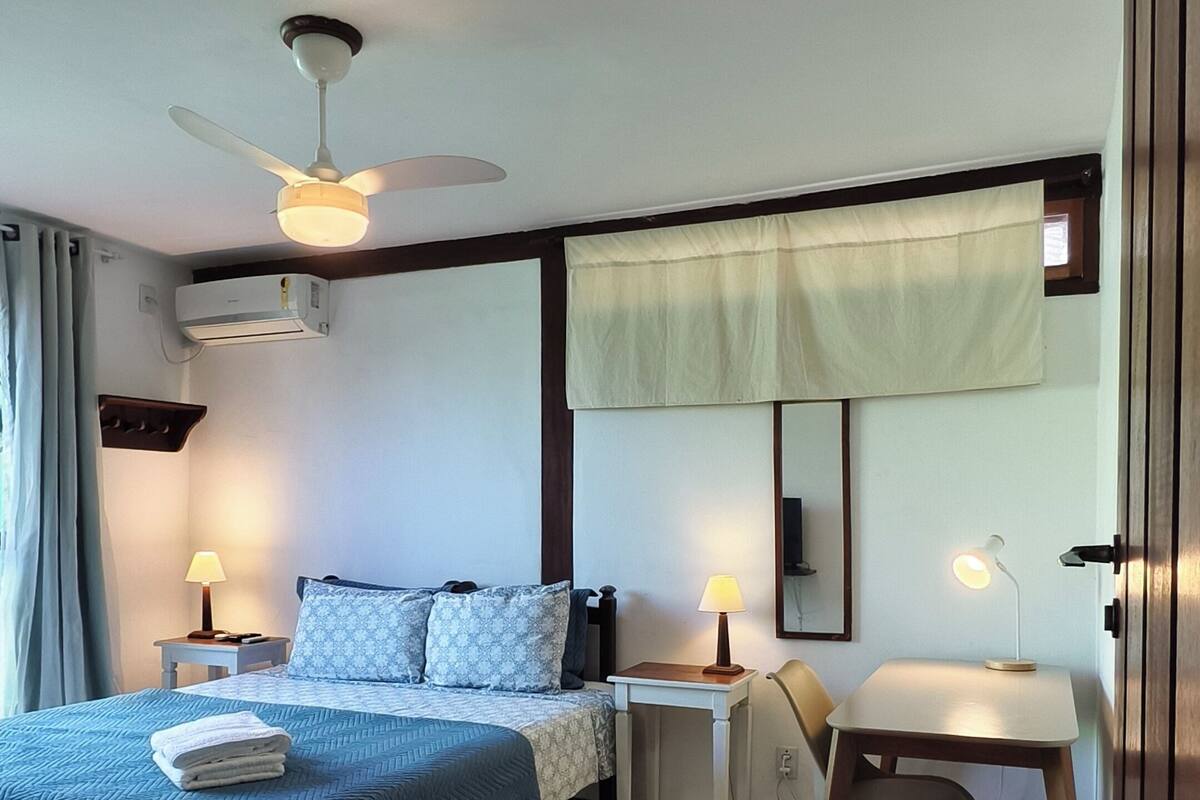 Un dormitorio con cama, mesitas de noche, un escritorio, un ventilador de techo y un equipo de aire acondicionado.