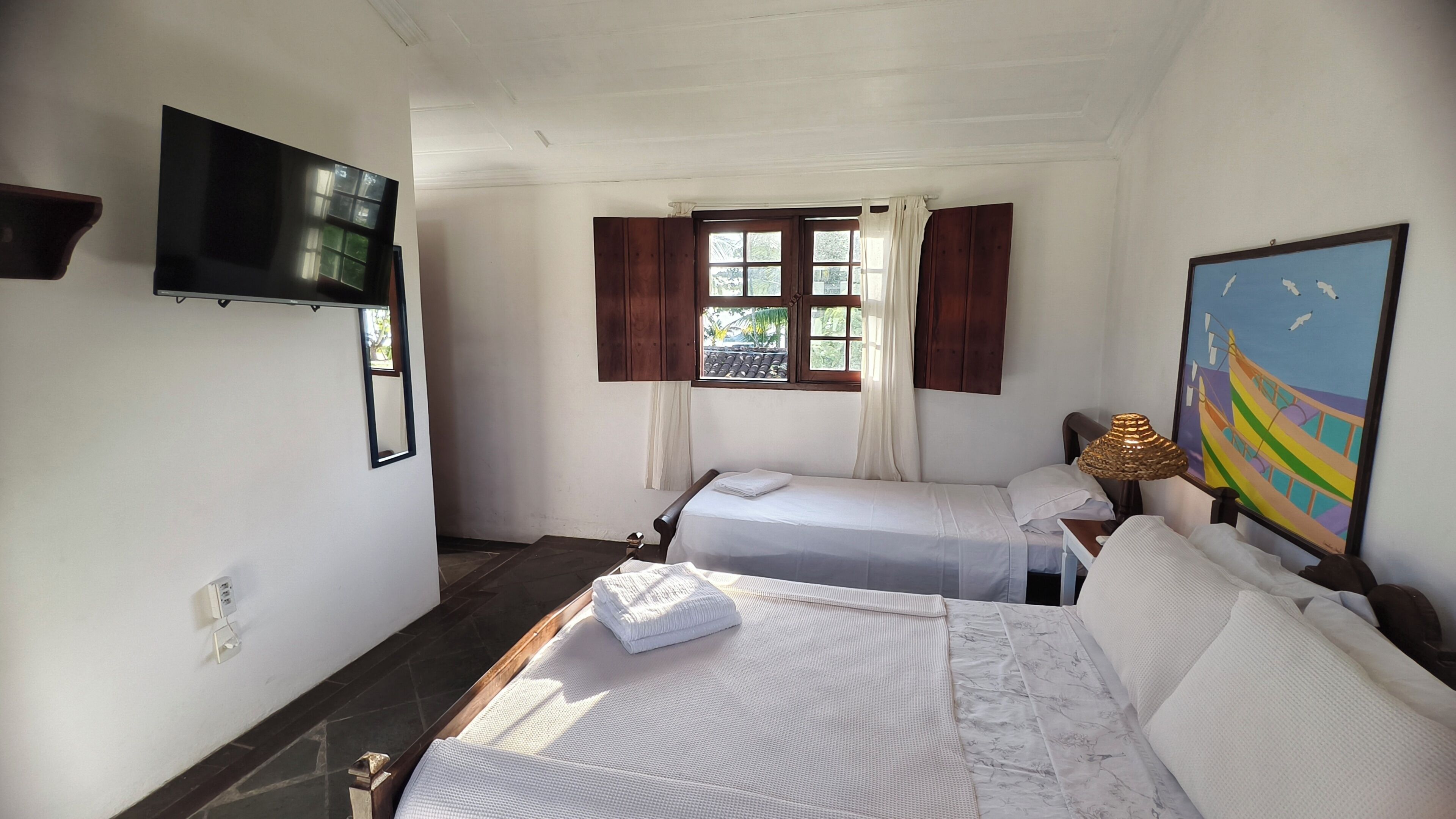 Ein Zimmer mit zwei Betten, einem an der Wand befestigten Fernseher, einem Fenster mit Vorhängen und einem Bild.