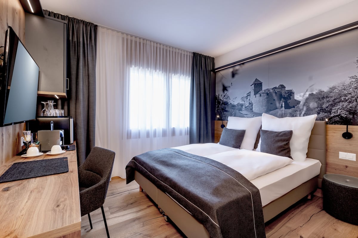 Une chambre d’hôtel équipée d  ’un lit, d’un bureau, d’une chaise, d’une télévision et d’une grande fenêtre avec des rideaux.