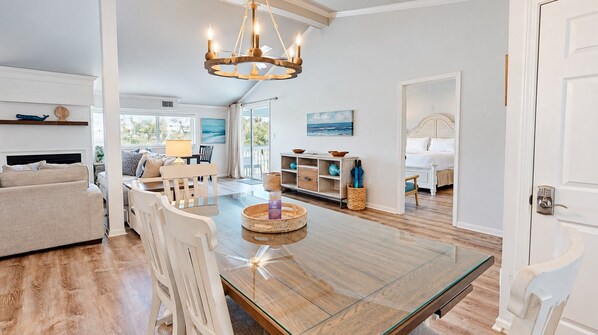 A spacious living area with a glass-top dining table, a chandelier, and a view of the outdoors.