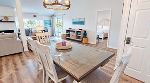 A spacious living area with a dining table, chairs, and a sofa. There is a fireplace, a bookshelf, and a painting on the wall.