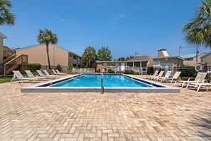 A rectangular swimming pool with a metal ladder, surrounded by lounge chairs and a brick patio.