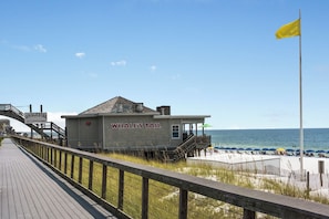 A boardwalk leading to a building labeled 'Whale's Tail Restaurant' with a beach and umbrellas in the background.