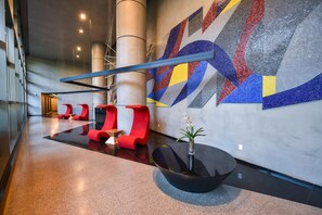 Eine moderne Lobby mit einem geometrischen Wandbild, roten Sitzgelegenheiten und einem schwarzen Tisch mit einer Vase.