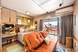 Habitación de hotel moderna con una cama grande, un escritorio, una silla, una hamaca y vistas a la ciudad.
